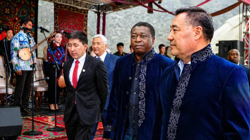 Faure Gnassingbé, in an embroidered Kyrgyz robe, walks with Kyrgyz officials past traditional musicians during his April 2026 visit to Kyrgyzstan.